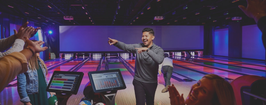 Excited bowler celebrating a strike with friends at colorful HyperBowling lanes at Outta Boundz